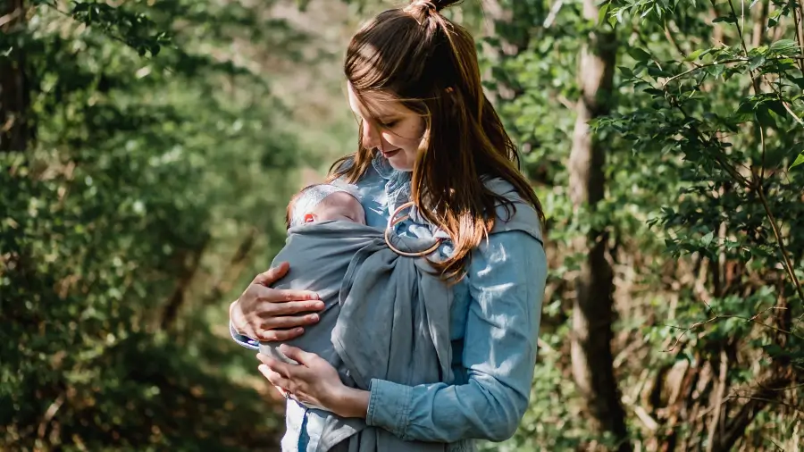 Mama trägt ihr Neugebornes im selbstgenähten Ring Sling durch den Wald