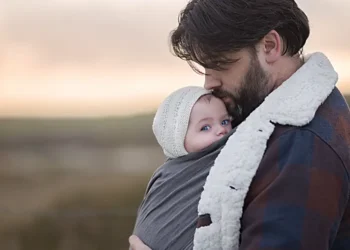 Ein Vater trägt sein Baby im Tragetuch im Winter unter seiner Jacke