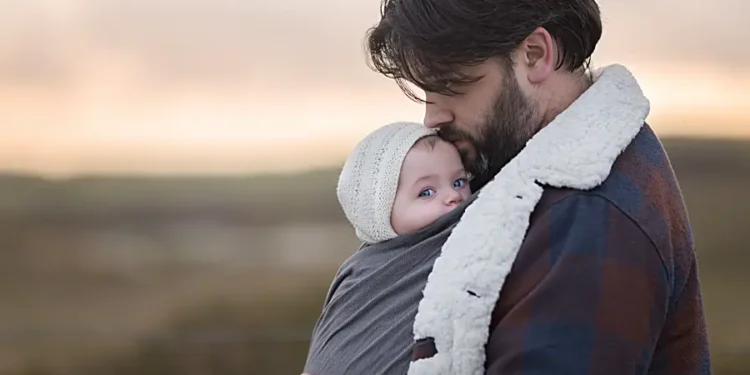 Ein Vater trägt sein Baby im Tragetuch im Winter unter seiner Jacke