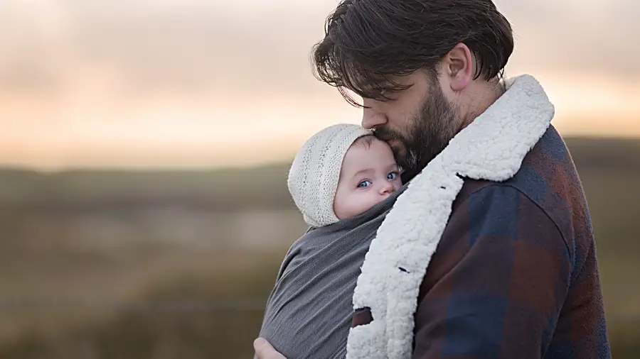 Ein Vater trägt sein Baby im Tragetuch im Winter unter seiner Jacke
