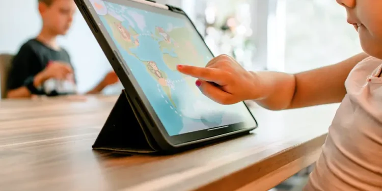 Etwa zweijähriges Kind sitz vor dem Tablet und spielt in einer App auf der eine Weltkarte und ein kleiner Affe zu sehen ist