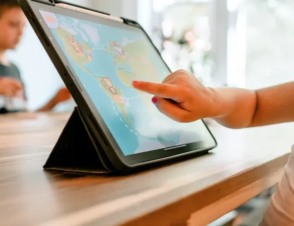 Etwa zweijähriges Kind sitz vor dem Tablet und spielt in einer App auf der eine Weltkarte und ein kleiner Affe zu sehen ist