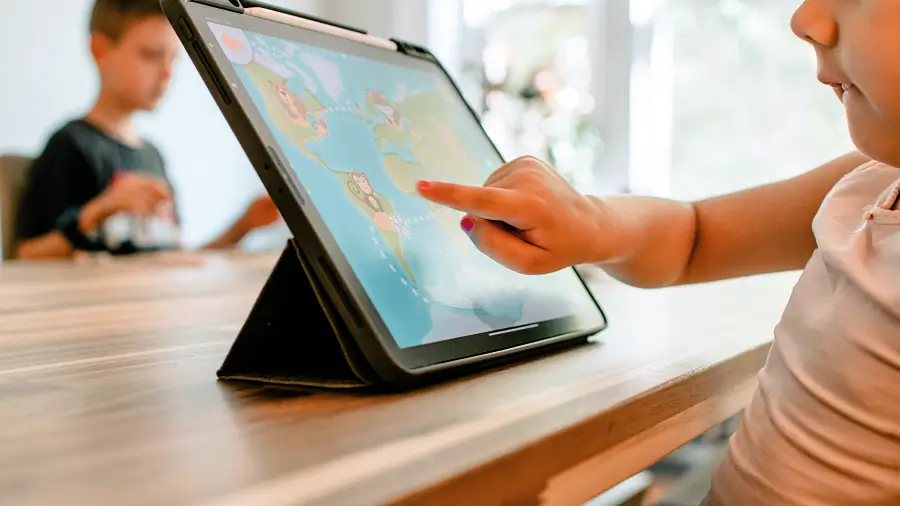 Etwa zweijähriges Kind sitz vor dem Tablet und spielt in einer App auf der eine Weltkarte und ein kleiner Affe zu sehen ist