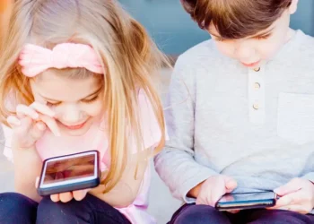 Zwei Kinder sitzen auf einer Treppe und spielen auf dem Smartphone